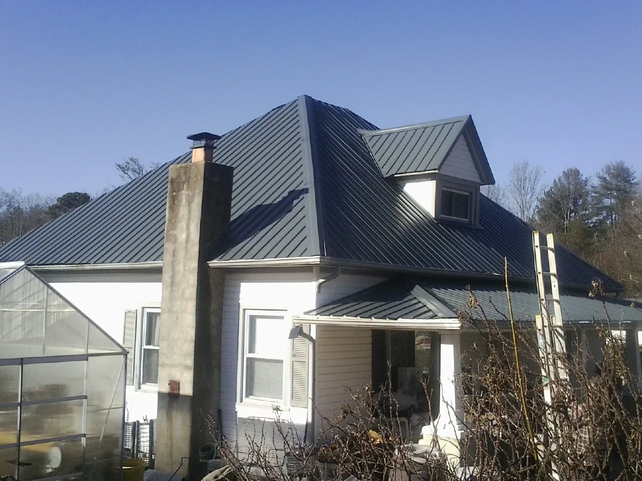 Dark blue standing seam metal roof on a white farmhouse with dormer — Slate & Tile Roof Repair by Roofing Brothers in Westfall