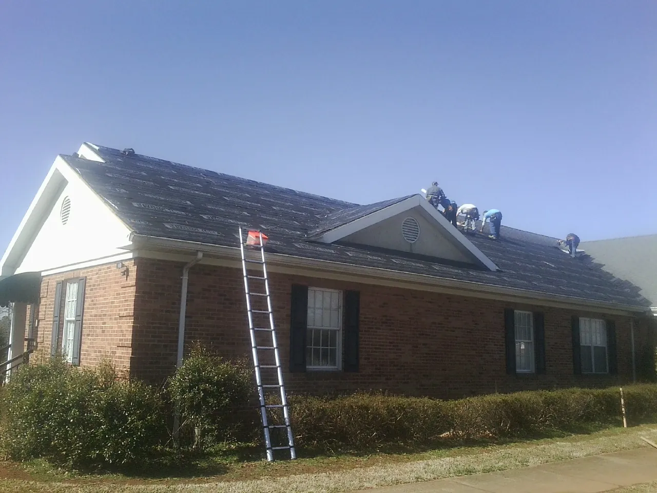 Crew tearing shingles off a brick ranch roof with a ladder set — Metal Roof Repair work by our crew in Westfall