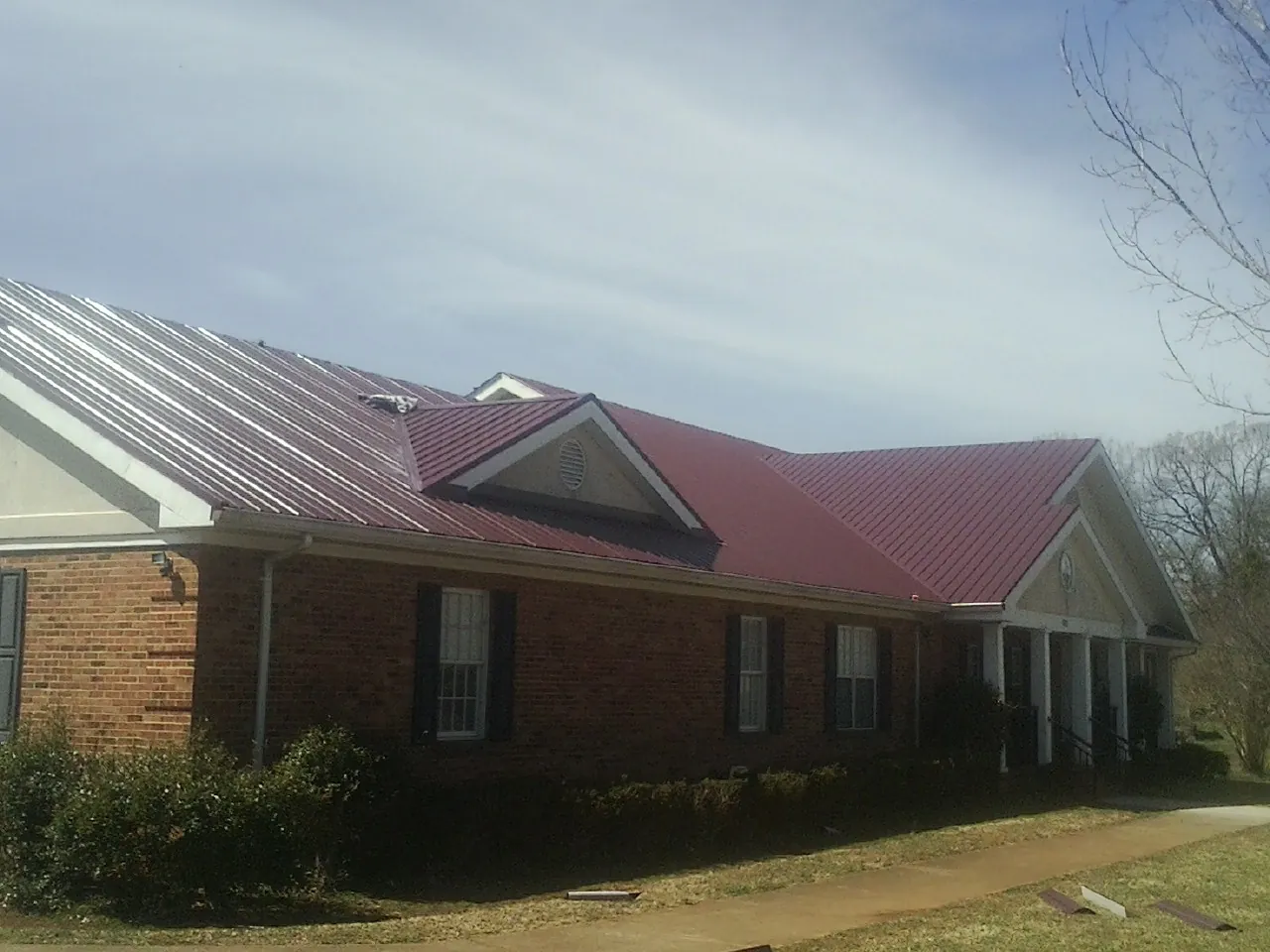 Red metal roof with gabled entries on a long brick building, from a Hail Damage Roof Repair job in Westfall