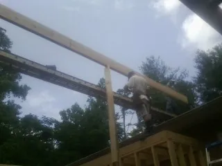 Carpenter setting a ridge beam over a new addition frame in Westfall