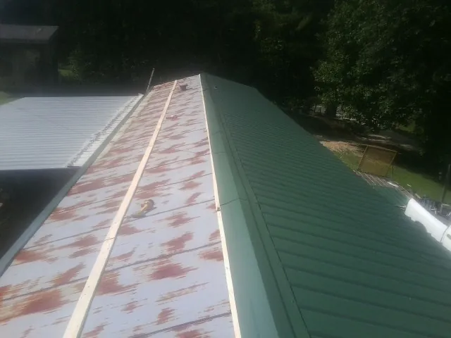 Old rusted panels beside newly installed green metal roofing — Wind Damage Roof Repair by Roofing Brothers in Westfall