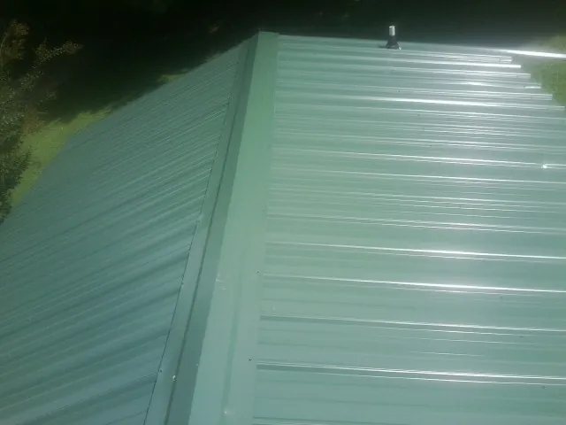 New green metal panels meeting at the ridge of a roof — Flat Roof Repair work by our crew in Westfall