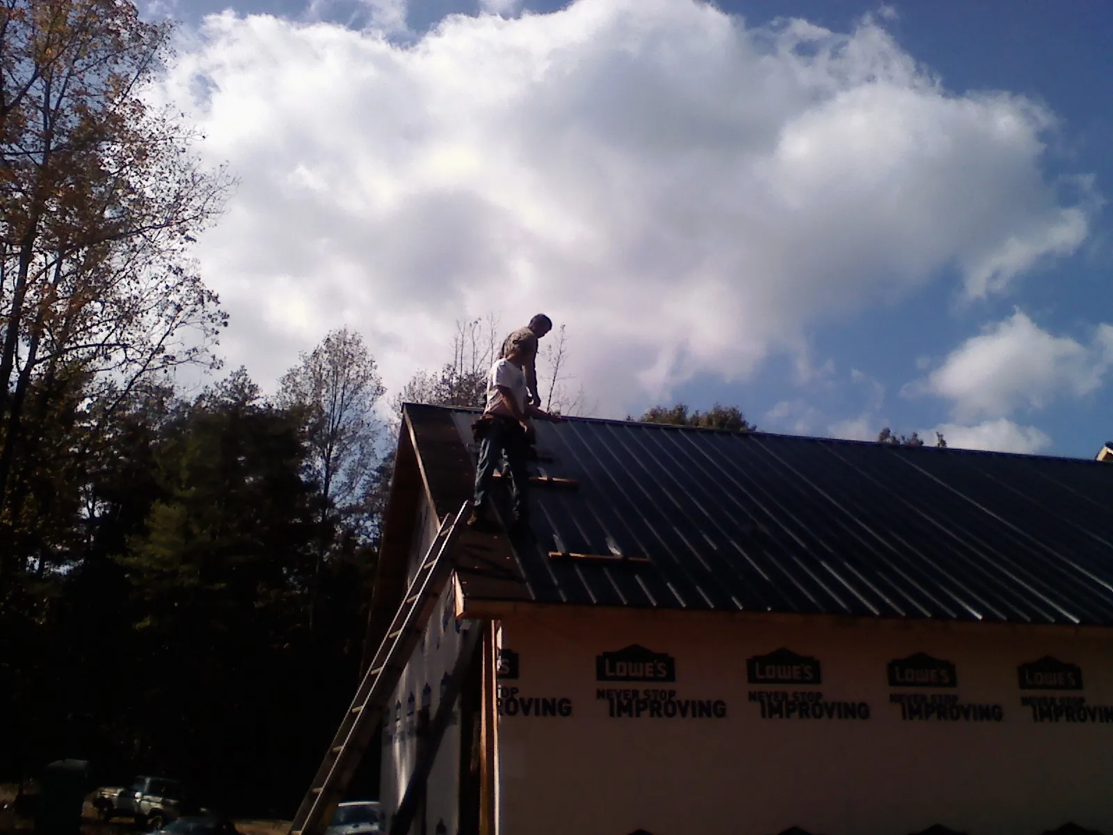Roofer fastening dark metal panels high against a cloudy sky, from a Roof Inspection job in Westfall